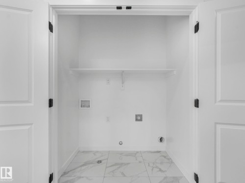 Dedicated laundry closet featuring a single built-in shelf, white panel doors, and white marble-look tile flooring - 239 Kinglet Boulevard Nw, Edmonton, AB - Indoor