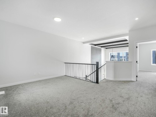 Expansive carpeted area featuring a prominent staircase with black metal railing, recessed lighting, and a modern ceiling detail above the stairwell - 239 Kinglet Boulevard Nw, Edmonton, AB - Indoor Photo Showing Other Room
