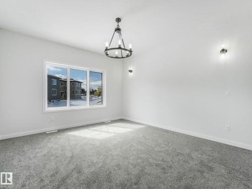 Expansive room featuring a large window, gray carpeting, a contemporary chandelier, and two wall sconces - 239 Kinglet Boulevard Nw, Edmonton, AB - Indoor Photo Showing Other Room