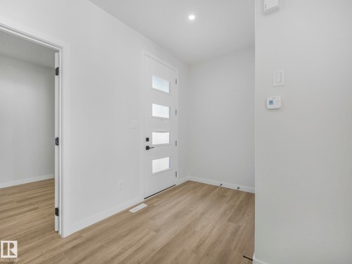 Entryway featuring a modern door with multiple frosted glass inserts, wood-finish flooring, recessed ceiling lighting, and a digital thermostat - 239 Kinglet Boulevard Nw, Edmonton, AB - Indoor Photo Showing Other Room