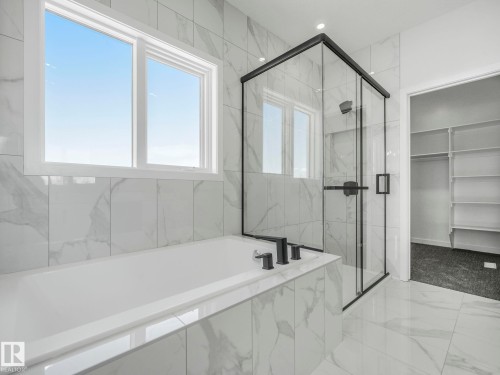 Modern bathroom featuring a built-in soaking tub with matte black fixtures, a frameless glass shower enclosure with matte black trim, and large format marble-look tile on walls and flooring - 239 Kinglet Boulevard Nw, Edmonton, AB - Indoor Photo Showing Bathroom
