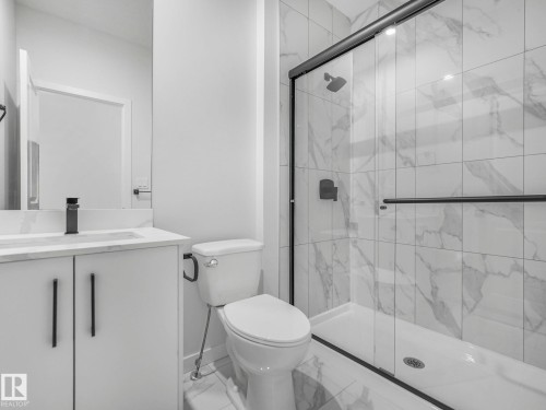Modern bathroom featuring a glass-enclosed shower with matte black fixtures, white marble-look subway tile, a white vanity with a rectangular sink, and a full-width mirror - 239 Kinglet Boulevard Nw, Edmonton, AB - Indoor Photo Showing Bathroom