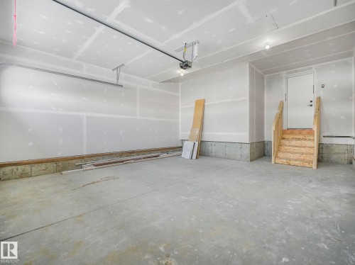 Spacious garage with exposed drywall, concrete flooring, and a single entry door with an unfinished wood staircase - 239 Kinglet Boulevard Nw, Edmonton, AB - Indoor Photo Showing Garage