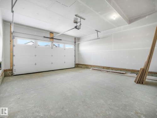 Spacious garage featuring a durable concrete floor, an automatic overhead door with integrated windows, and exposed ceiling joists - 239 Kinglet Boulevard Nw, Edmonton, AB - Indoor Photo Showing Garage
