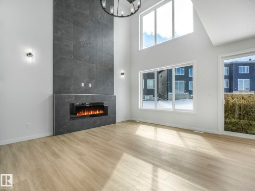 Two-story living area featuring a full-height tiled fireplace, electric linear fireplace, wood-finish flooring, and a black chandelier - 239 Kinglet Boulevard Nw, Edmonton, AB - Indoor With Fireplace