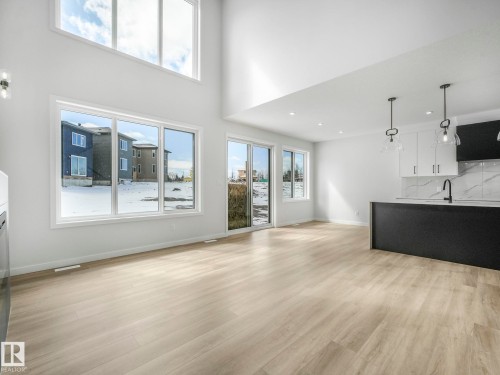 Open-concept living space featuring wood-finish flooring, a two-story ceiling, and a kitchen island with pendant lighting - 239 Kinglet Boulevard Nw, Edmonton, AB - Indoor