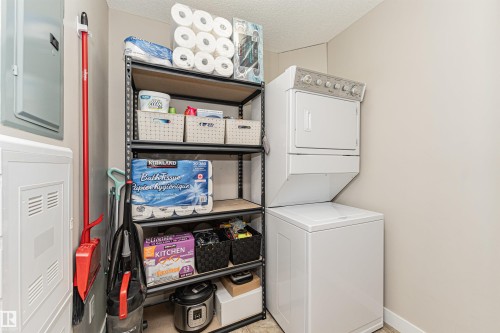 Stackable washer and dryer appliances, shelving unit, and wall-mounted electrical panels - #310 2229 44 Av Nw, Edmonton, AB - Indoor Photo Showing Laundry Room