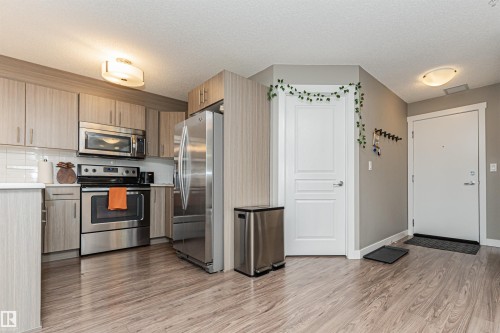Kitchen featuring stainless steel appliances, wood-finish cabinetry, white subway tile backsplash, and light countertops - #310 2229 44 Av Nw, Edmonton, AB - Indoor Photo Showing Kitchen