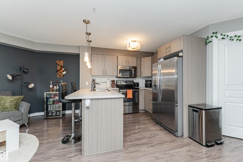 Kitchen featuring light wood-finish cabinetry, stainless steel appliances, and an island with bar seating - #310 2229 44 Av Nw, Edmonton, AB - Indoor Photo Showing Kitchen