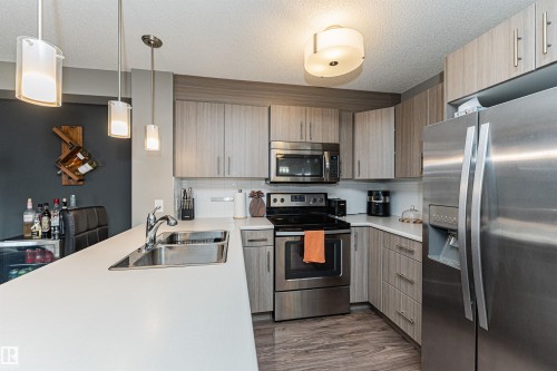 Modern kitchen featuring stainless steel appliances, wood-finish cabinetry, a large kitchen island with an undermount sink, and recessed lighting - #310 2229 44 Av Nw, Edmonton, AB - Indoor Photo Showing Kitchen With Double Sink