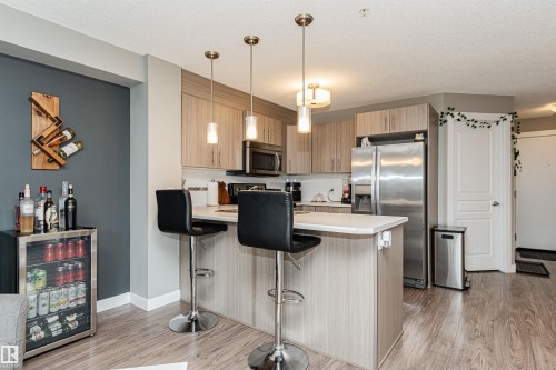 Modern kitchen featuring light wood-finish cabinetry, stainless steel appliances, and a white quartz countertop island with seating for two - #310 2229 44 Av Nw, Edmonton, AB - Indoor Photo Showing Kitchen