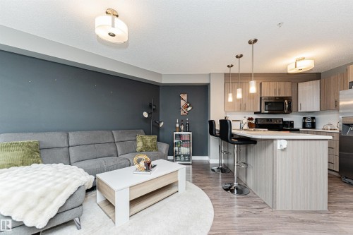 Open-concept living area with wood-finish flooring, a kitchen island with seating, pendant lighting, and contemporary cabinetry - #310 2229 44 Av Nw, Edmonton, AB - Indoor Photo Showing Kitchen