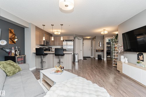Open-concept living area with wood-finish flooring, recessed lighting, and a kitchen featuring stainless steel appliances - #310 2229 44 Av Nw, Edmonton, AB - Indoor Photo Showing Living Room