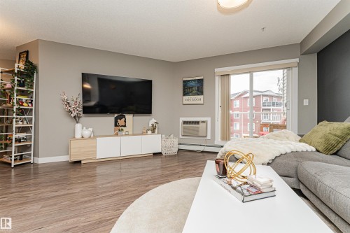 Spacious open-concept living area showcasing wood-finish flooring throughout, a wall-mounted flat-screen television, and built-in cabinetry with ample storage - #310 2229 44 Av Nw, Edmonton, AB - Indoor Photo Showing Living Room