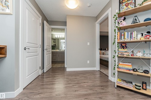 Bright hallway with neutral wall finishes, wood-finish flooring throughout, recessed ceiling lighting, and custom built-in shelving with wooden frames displaying décor and collectibles - #310 2229 44 Av Nw, Edmonton, AB - Indoor Photo Showing Other Room