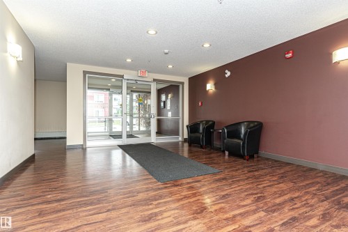 Wood-finish flooring with a dark accent wall and modern sconce lighting - #310 2229 44 Av Nw, Edmonton, AB - Indoor Photo Showing Other Room