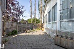 Paved patio area, wood fencing, and a white-sided structure with multiple windows - 