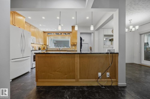 Modern kitchen featuring warm wood cabinetry with glass-front upper cabinets, stainless steel appliances, granite countertops, and a substantial wood-finish island with pendant lighting - 9503 54 Street Nw, Edmonton, AB - Indoor Photo Showing Kitchen