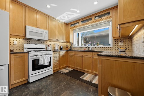 Light wood-finish cabinetry, black stone countertops, white appliances, patterned tile backsplash, and recessed lighting - 9503 54 Street Nw, Edmonton, AB - Indoor Photo Showing Kitchen