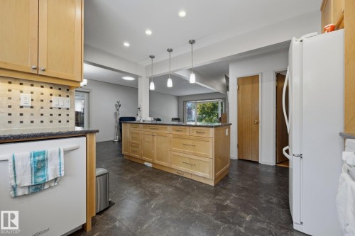 Modern kitchen featuring natural wood cabinetry with brushed metal hardware, stainless steel appliances, quartz countertops, a large center island with seating, pendant lighting, and dark tile flooring throughout the open-concept space - 9503 54 Street Nw, Edmonton, AB - Indoor Photo Showing Kitchen