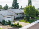 Modern home featuring a two-car garage with paneled doors, metal roof with architectural shingles, and a professionally landscaped front yard with mature trees, manicured lawn, and tiered planting beds - 9503 54 Street Nw, Edmonton, AB 