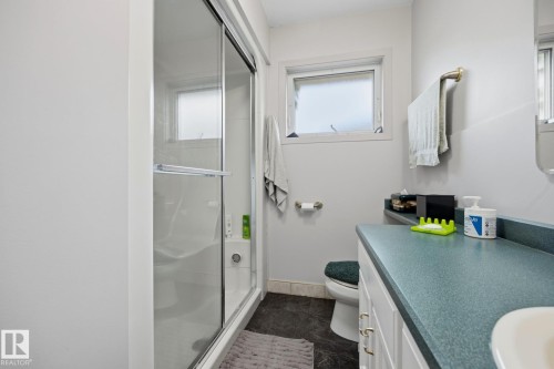 Enclosed shower with glass sliding door, vanity with integrated sink, white cabinetry with brass hardware, and a small window - 9503 54 Street Nw, Edmonton, AB - Indoor Photo Showing Bathroom