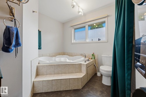 Master bathroom featuring a corner soaking tub with tile surround, separate toilet, pedestal sink with chrome fixtures, tile flooring, and natural light from dual windows with privacy glass - 9503 54 Street Nw, Edmonton, AB - Indoor Photo Showing Bathroom