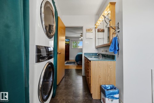 Stacked laundry appliances, wood-finish vanity with countertop, integrated sink, and mirrored medicine cabinet - 9503 54 Street Nw, Edmonton, AB - Indoor Photo Showing Laundry Room