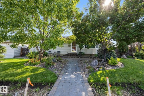Manicured front lawn with mature trees, a paver pathway, and garden beds with decorative rocks - 9503 54 Street Nw, Edmonton, AB - Outdoor