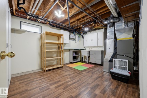 Basement utility area featuring wood-finish flooring, exposed ceiling joists, white cabinetry, a utility sink, and HVAC systems - 9503 54 Street Nw, Edmonton, AB - Indoor Photo Showing Basement