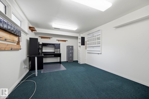 Dedicated office space featuring built-in cabinetry with wood-finish shelving, professional-grade printer and equipment setup, teal carpeting, bright overhead lighting, and wall-mounted organizational systems - 9503 54 Street Nw, Edmonton, AB - Indoor Photo Showing Other Room