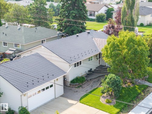 Modern residence featuring a newly installed metal roof with architectural standing seam detailing, attached two-car garage with paneled doors, and mature landscaping including evergreen trees and manicured lawn - 9503 54 Street Nw, Edmonton, AB - Outdoor With Exterior