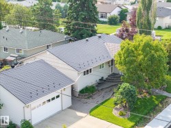 Modern residence featuring a newly installed metal roof with architectural standing seam detailing, attached two-car garage with paneled doors, and mature landscaping including evergreen trees and manicured lawn - 