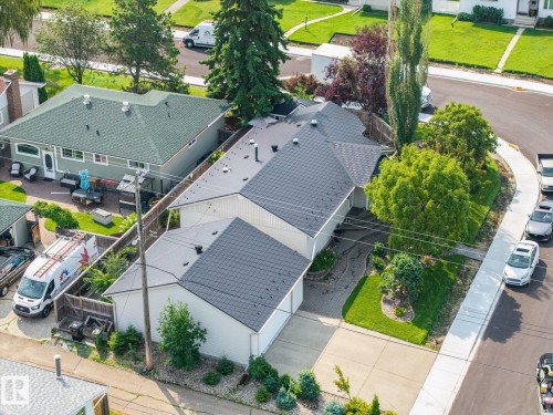 Modern residence featuring a distinctive multi-pitched architectural design with dark asphalt shingle roofing, clean white exterior siding, and professional landscaping with mature greenery throughout the front grounds - 9503 54 Street Nw, Edmonton, AB - Outdoor