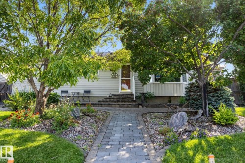 Paver stone walkway leading to a front entry, featuring mature trees, diverse landscaping with natural stone elements, and a bay window - 9503 54 Street Nw, Edmonton, AB - Outdoor