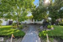 Manicured front lawn with mature trees, a paver pathway, and garden beds with decorative rocks - 9503 54 Street Nw, Edmonton, AB 