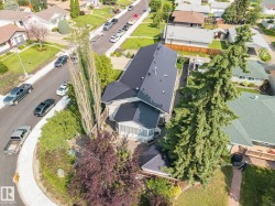 Modern residence featuring a striking black pitched roof, mature landscaping with evergreen and ornamental trees, and a curved driveway approach - 