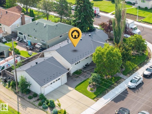 Charming single-story residence featuring a freshly resurfaced dark gray asphalt shingle roof, detached two-car garage with matching roofline, and mature landscaping including tall evergreen trees and manicured lawn - 9503 54 Street Nw, Edmonton, AB - Outdoor