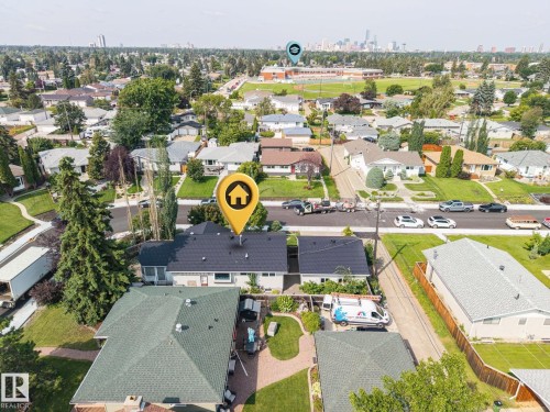 Aerial view showcasing this residential property featuring a dark-shingle roof, manicured lawn with mature landscaping, brick and stone exterior finishes, and a driveway with parking - 9503 54 Street Nw, Edmonton, AB - Outdoor With View