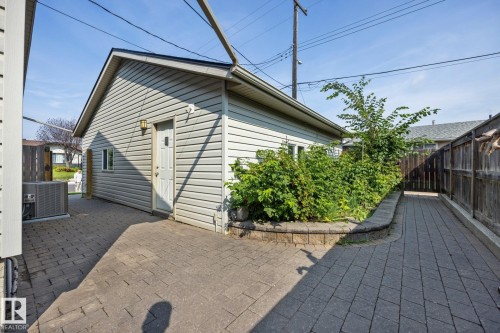 Spacious paved patio with permeable pavers extending across the backyard, complemented by mature landscaping and vinyl-sided cottage structure with peaked roofline - 9503 54 Street Nw, Edmonton, AB - Outdoor