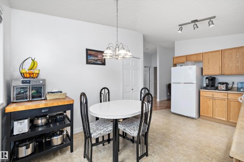 Kitchen and dining area featuring light wood-finish cabinetry, a white refrigerator, and a track light fixture - 3344 24 Avenue Nw, Edmonton, AB - Indoor