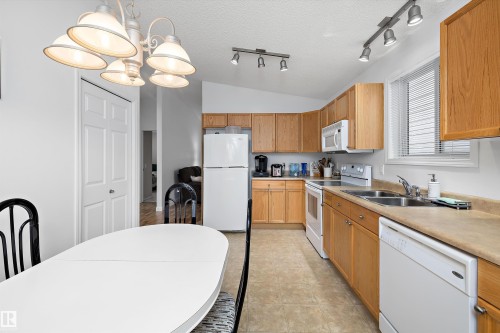 Kitchen and dining area featuring wood-finish cabinetry, a window with blinds, stainless steel double basin sink, and an overhead chandelier - 3344 24 Avenue Nw, Edmonton, AB - Indoor Photo Showing Kitchen With Double Sink