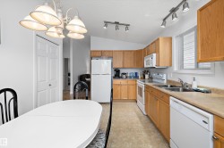 Kitchen and dining area featuring wood-finish cabinetry, a window with blinds, stainless steel double basin sink, and an overhead chandelier - 