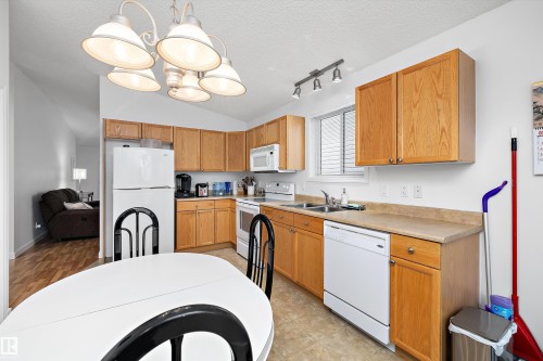 Kitchen featuring light wood cabinetry, white appliances, laminate countertops, a double basin sink, and track lighting - 3344 24 Avenue Nw, Edmonton, AB - Indoor Photo Showing Kitchen With Double Sink