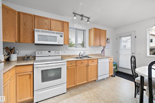 Kitchen featuring light wood cabinetry, white appliances, a double basin sink, track lighting, and a light-toned flooring - 3344 24 Avenue Nw, Edmonton, AB - Indoor Photo Showing Kitchen With Double Sink