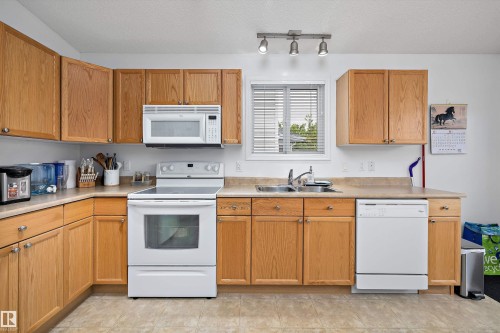 Kitchen featuring wood-finish cabinetry, white appliances, laminate countertops, and a window with blinds - 3344 24 Avenue Nw, Edmonton, AB - Indoor Photo Showing Kitchen With Double Sink