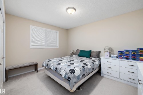 Carpeted bedroom with a window featuring white blinds, neutral wall tones, and a ceiling-mounted light fixture - 3344 24 Avenue Nw, Edmonton, AB - Indoor Photo Showing Bedroom