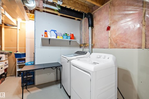 Dedicated laundry area featuring a washer and dryer, an exposed wood beam ceiling, and a wall-mounted shelving unit - 3344 24 Avenue Nw, Edmonton, AB - Indoor Photo Showing Laundry Room