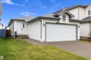 White siding exterior featuring an attached two-car garage, concrete driveway, front entry with a sidelight, and a peaked dormer accent - 3344 24 Avenue Nw, Edmonton, AB  - Outdoor With Exterior 