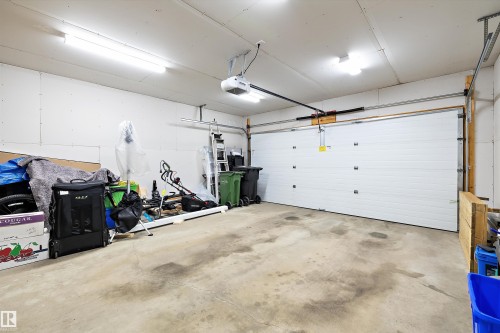 Spacious garage featuring a white panel garage door with an automatic opener, exposed drywall walls, and overhead fluorescent lighting - 3344 24 Avenue Nw, Edmonton, AB - Indoor Photo Showing Garage
